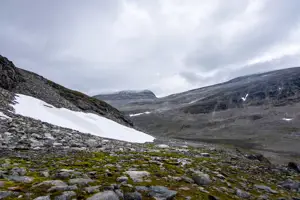 Smältande glaciär på ett berg. I bakgrunden syns flera berg. Det är gråmulet väder.