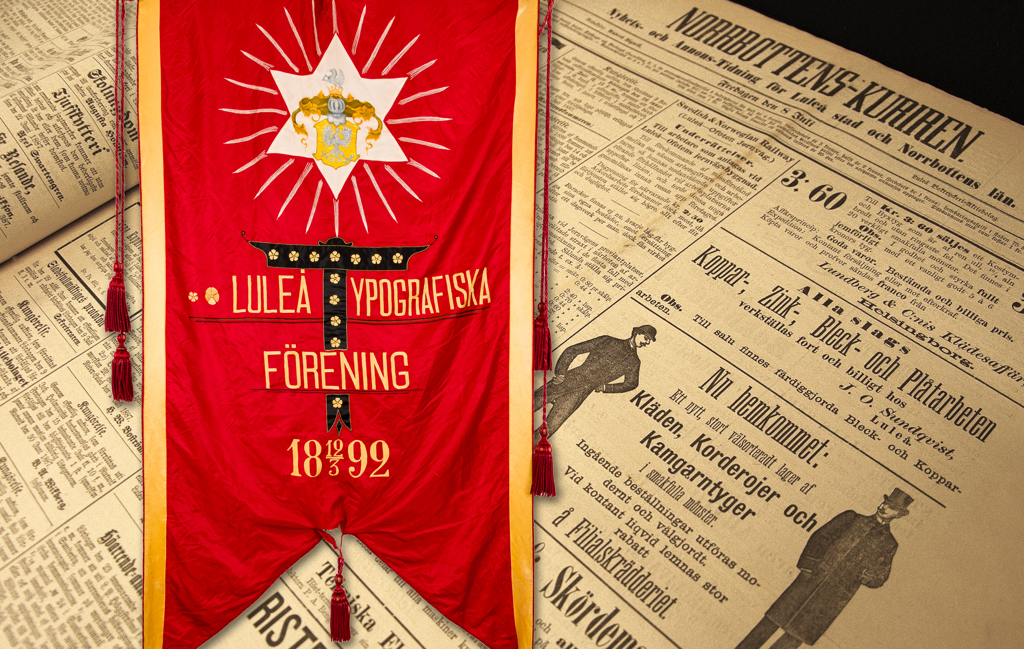 Ett äldre uppslag av Norrbottens-Kuriren, samt en fana med texten "Luleå Typografiska Förening 1892".