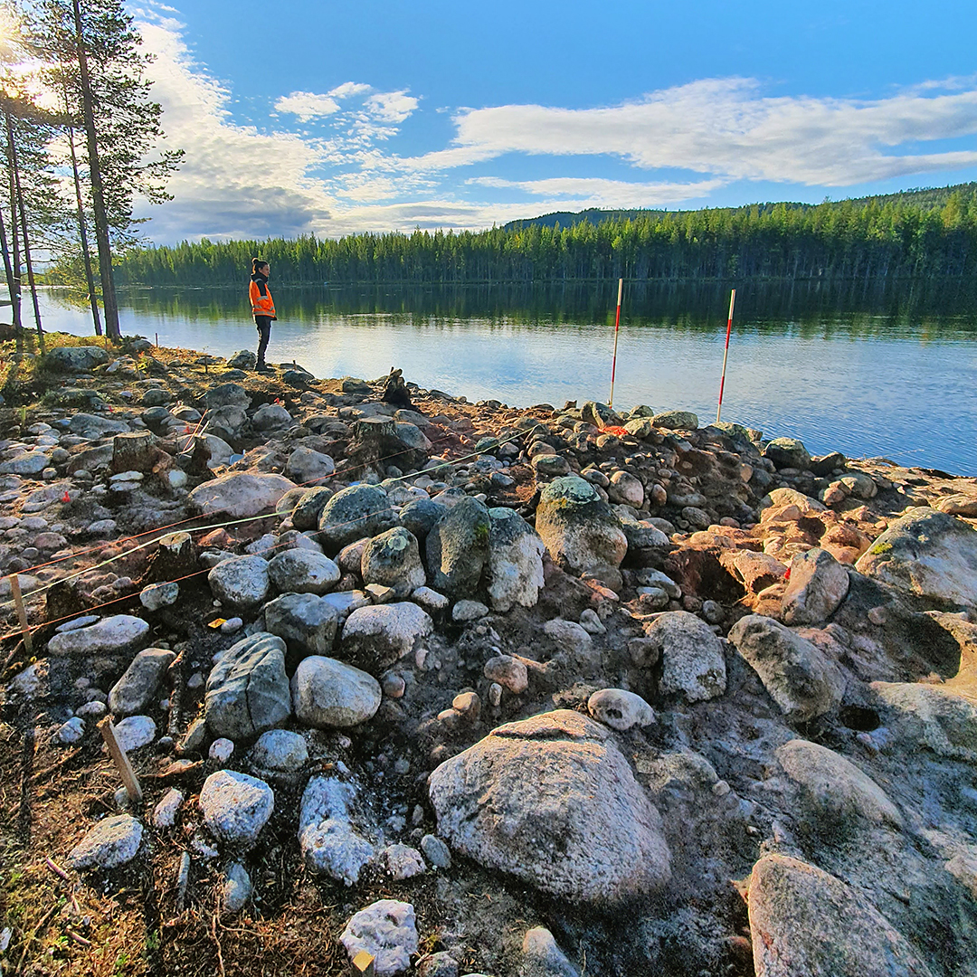 'En arkeolog som står på en stenig mark intill en älv.'